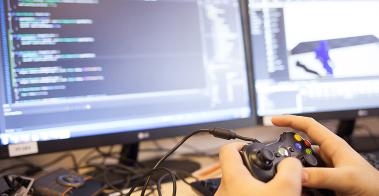 Game programming student testing their project using a game controller connected to a desktop computer.