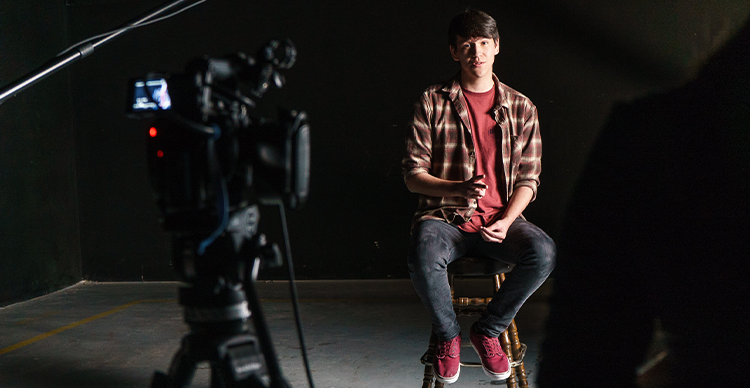 An actor performs an on-camera audition or self-tape in a professional studio environment, speaking directly toward the camera.